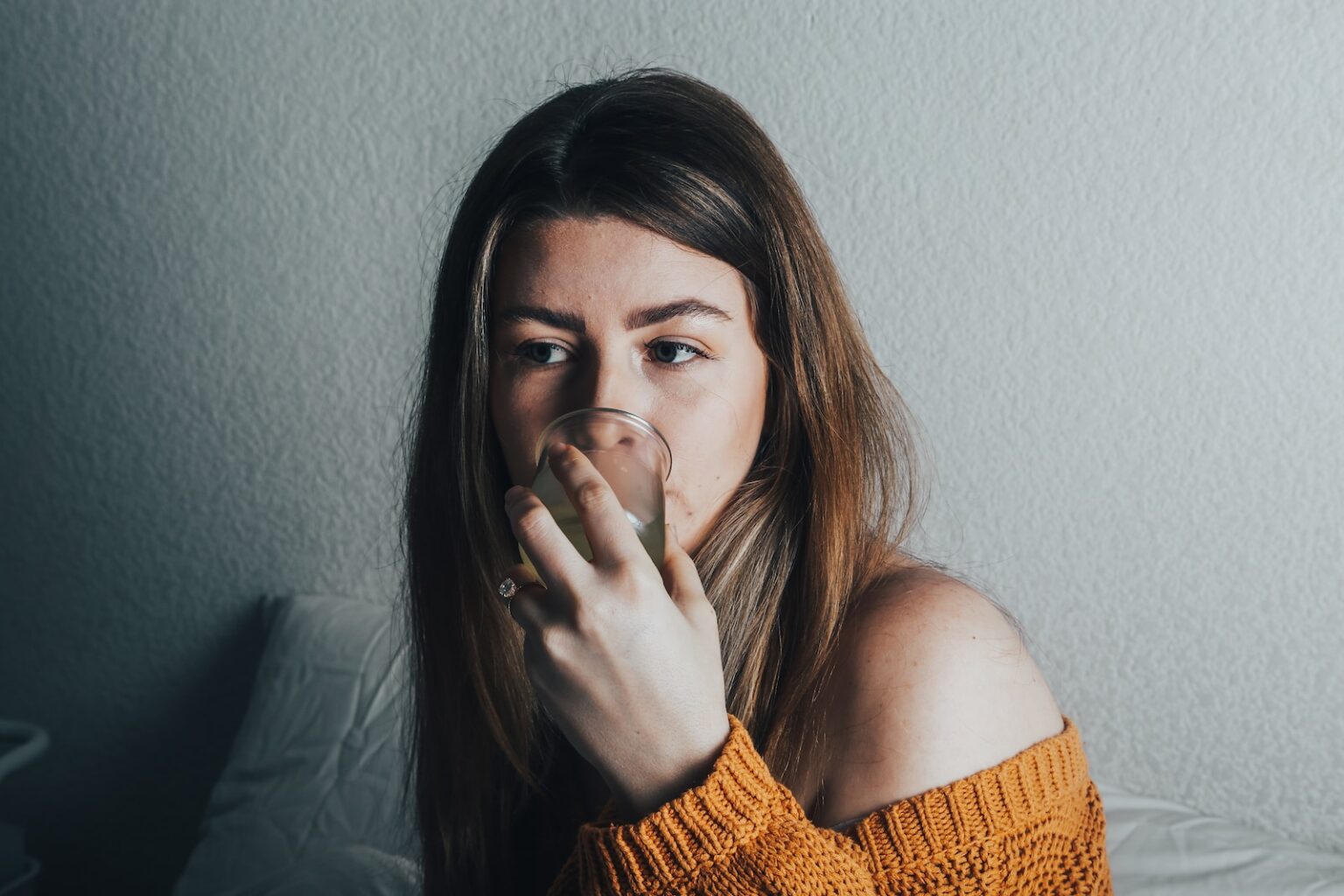 a woman in an orange sweater drinking from a glass