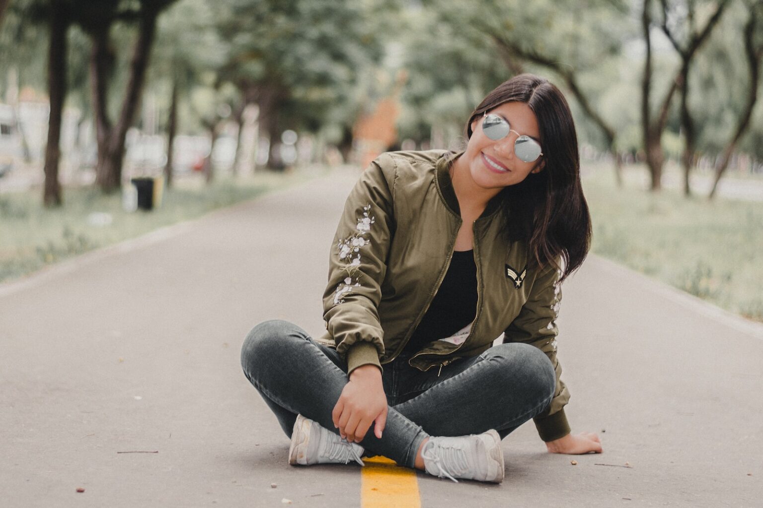 woman in brown jacket and blue denim jeans sitting on gray concrete floor during daytime