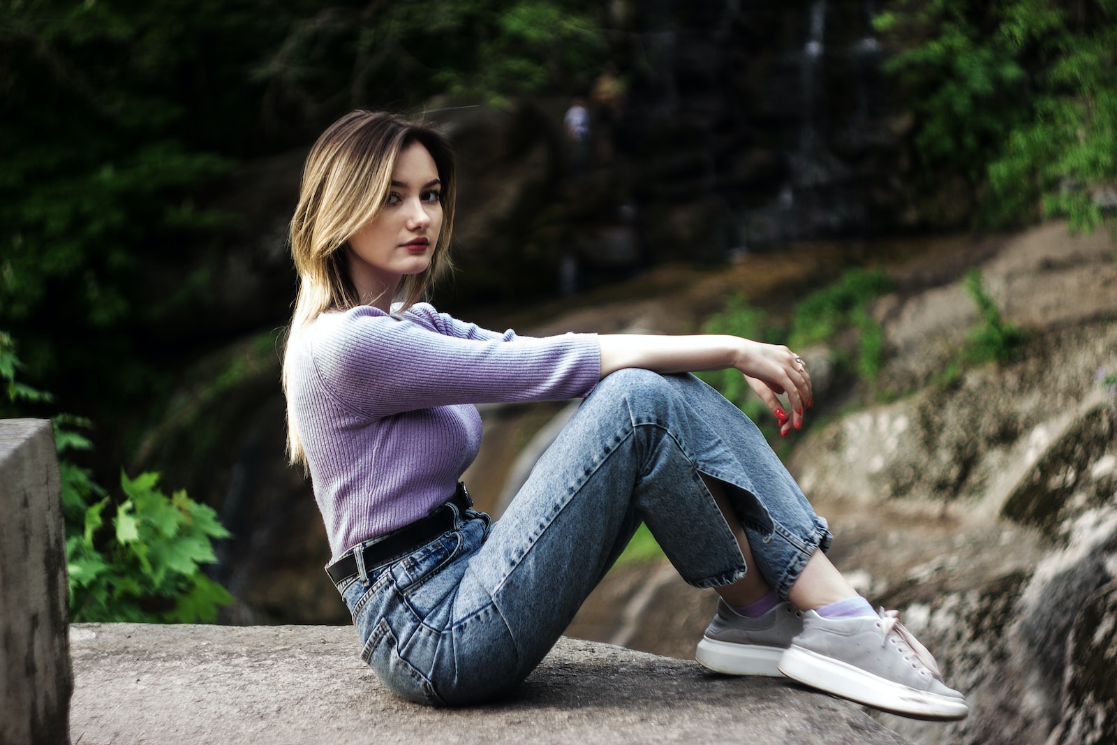 woman in white sweater and blue denim jeans sitting on concrete bench during daytime